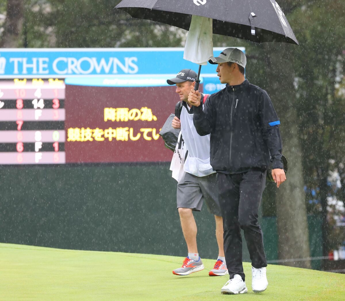 降雨のため試合が中断され、傘をさして１８番グリーンの横を通りクラブハウスへ戻る中島啓太　（カメラ・豊田　秀一）